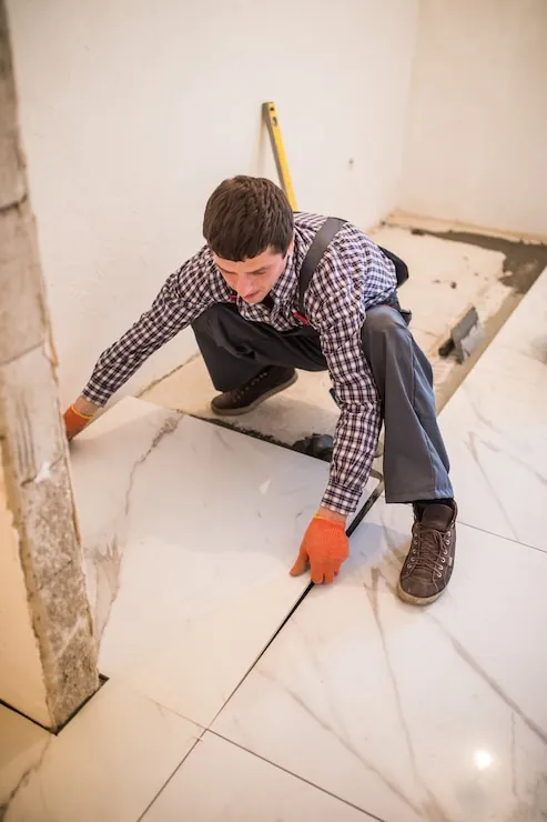 A tiler laying large floor tiles on adhesive in a flat being renovated